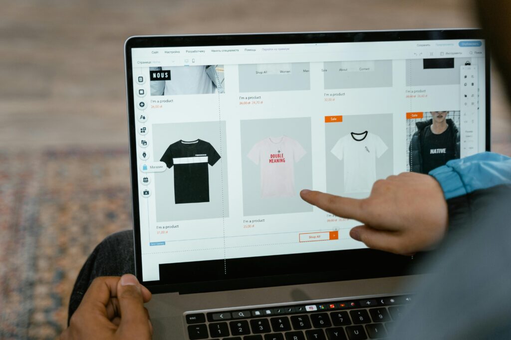 A person points to t-shirt options in an online store on a laptop screen.